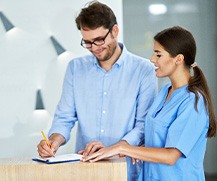 Man signing paperwork at dental office front desk